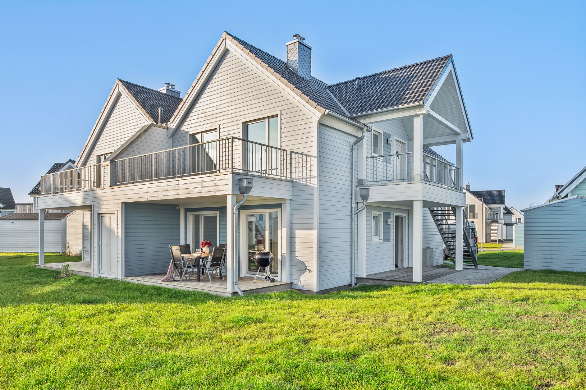 Modernes zweistöckiges Haus mit Balkon, Terrasse und Sitzbereich auf grünem Rasen.