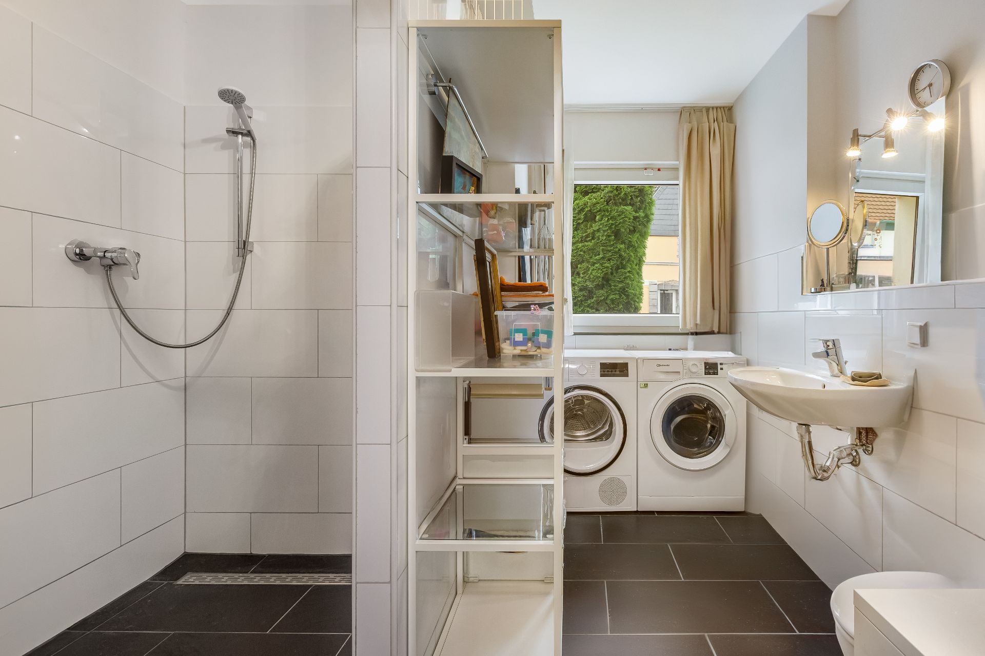 Modernes Badezimmer mit Dusche, Regal, Waschmaschine, Trockner, Waschbecken und Fenster.