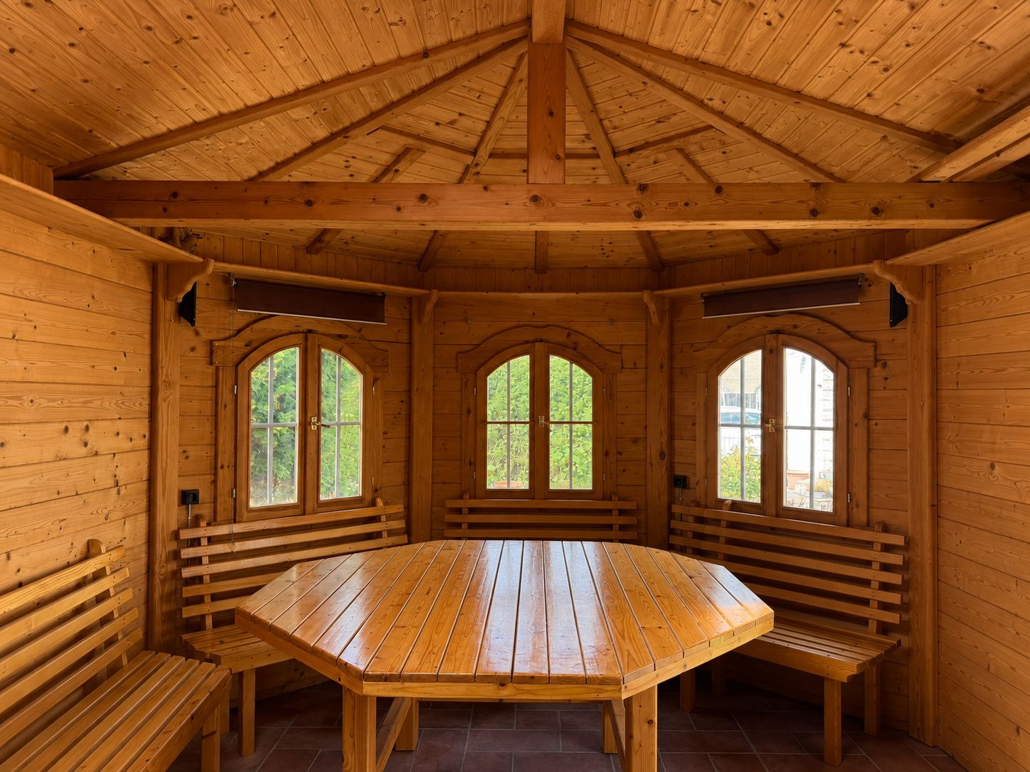 Holzpavillon mit achteckigem Tisch und Bänken, drei Fenster mit Blick nach draußen.