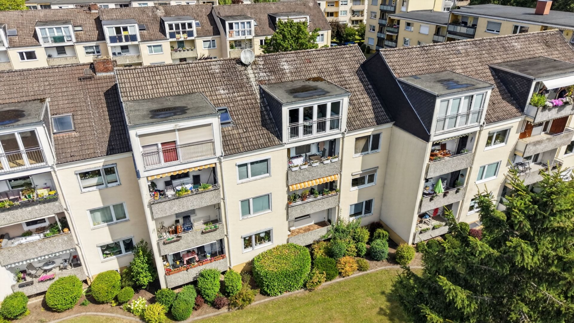 Mehrfamilienhaus mit Balkonen und gepflegtem Vorgarten, aufgenommen aus der Vogelperspektive.