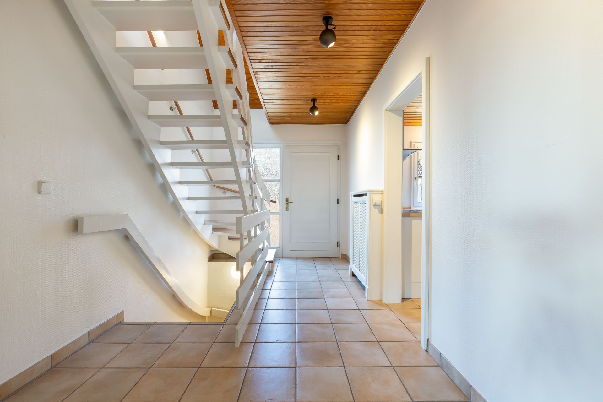 Heller Flur mit Treppe, Fliesenboden und Holzbalkendecke in einem Wohnhaus.