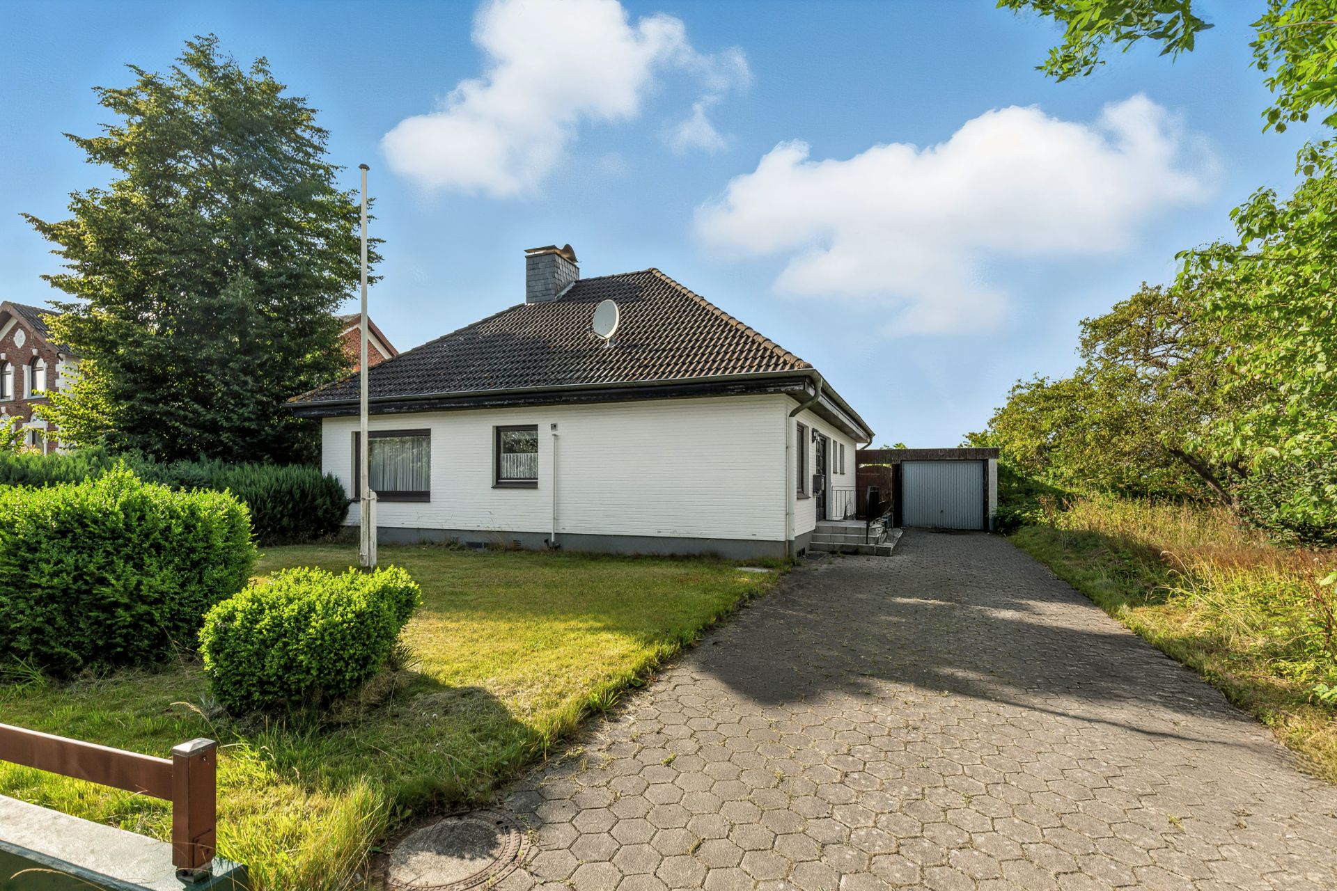 Einfamilienhaus mit dunklem Dach, Vorgarten und Einfahrt zu einer Garage.