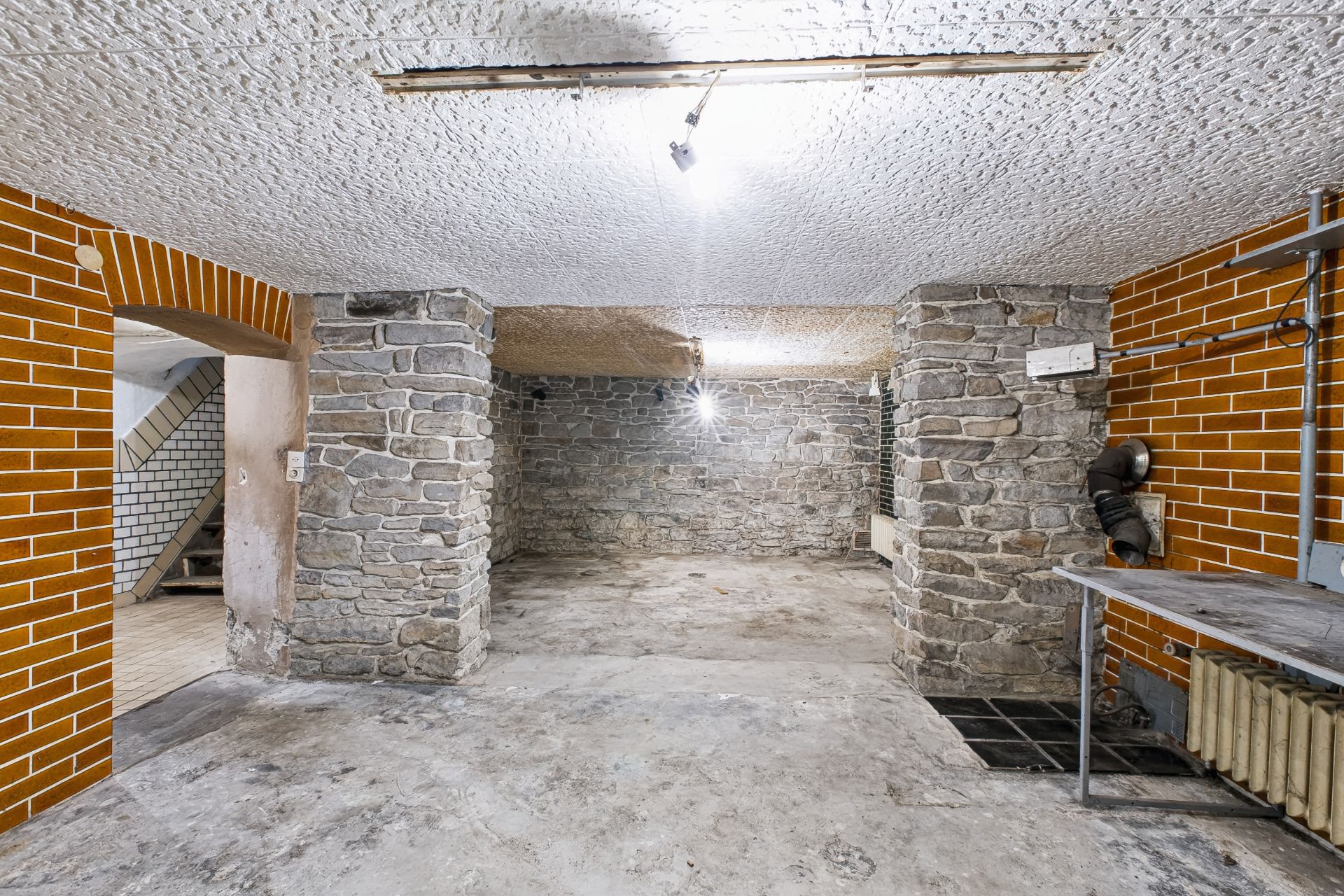 Kellerraum mit Steinwänden, Betonboden und einfachem Licht an der Decke.