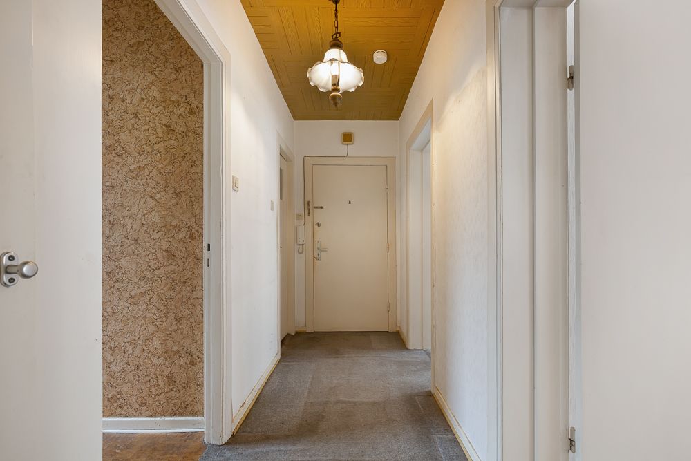 Flur mit Teppichboden, weißen Wänden, gelber Decke und einer Deckenlampe.