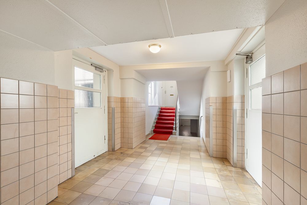 Heller Hausflur mit Fliesenboden, zwei Türen und Treppe mit rotem Teppich.