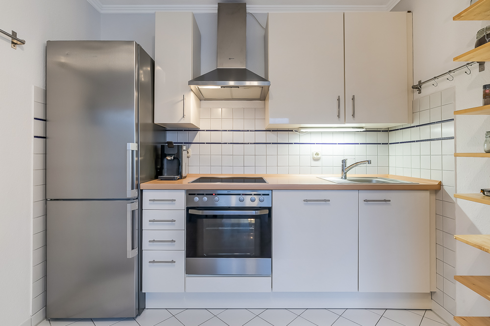 Moderne Einbauküche mit Edelstahlkühlschrank, Herd, Spüle und offenen Regalen an der Wand.