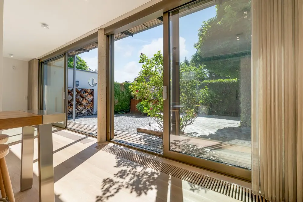 Helles Wohnzimmer mit großen Glasschiebetüren und Blick auf eine Terrasse mit Bäumen.