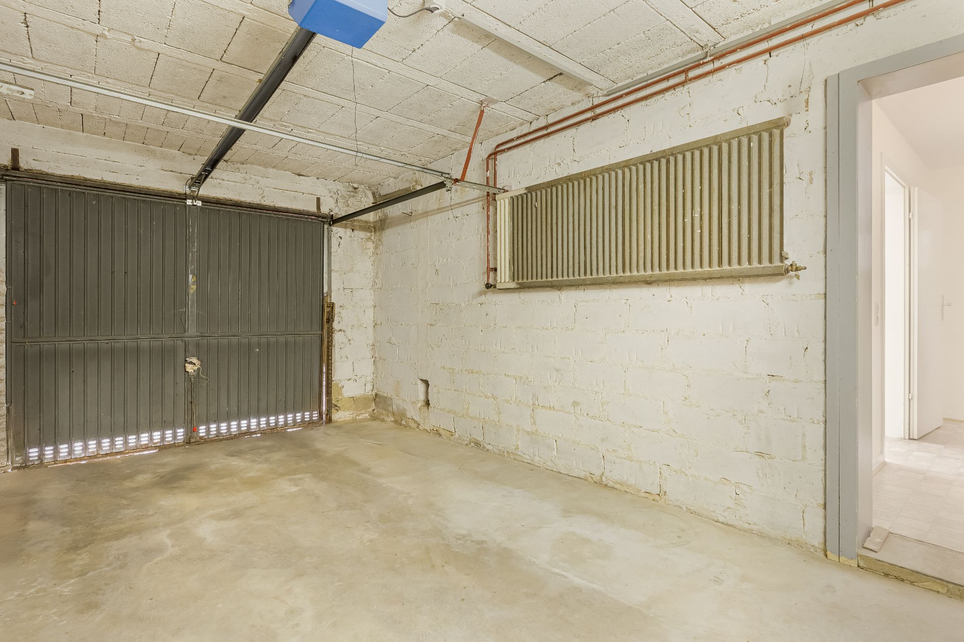 Leere Garage mit Betonboden, großem Tor und Zugangstür zum Haus.