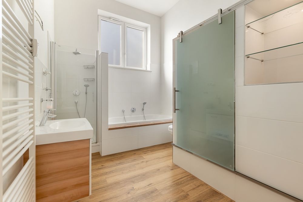 Modernes Badezimmer mit Badewanne, Dusche, Waschbecken und Holzfußboden.