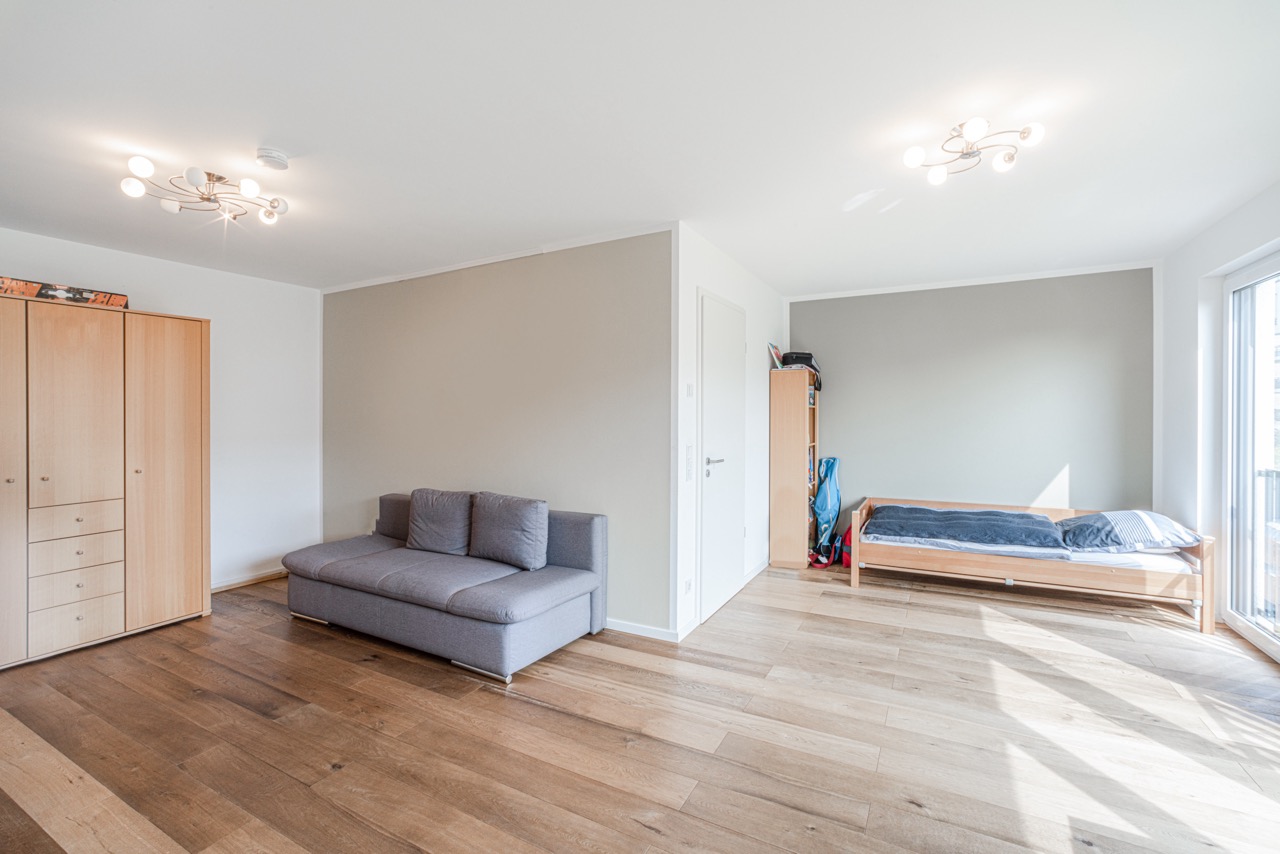 Helles Zimmer mit grauem Sofa, Einzelbett, Kleiderschrank und Holzfußboden.
