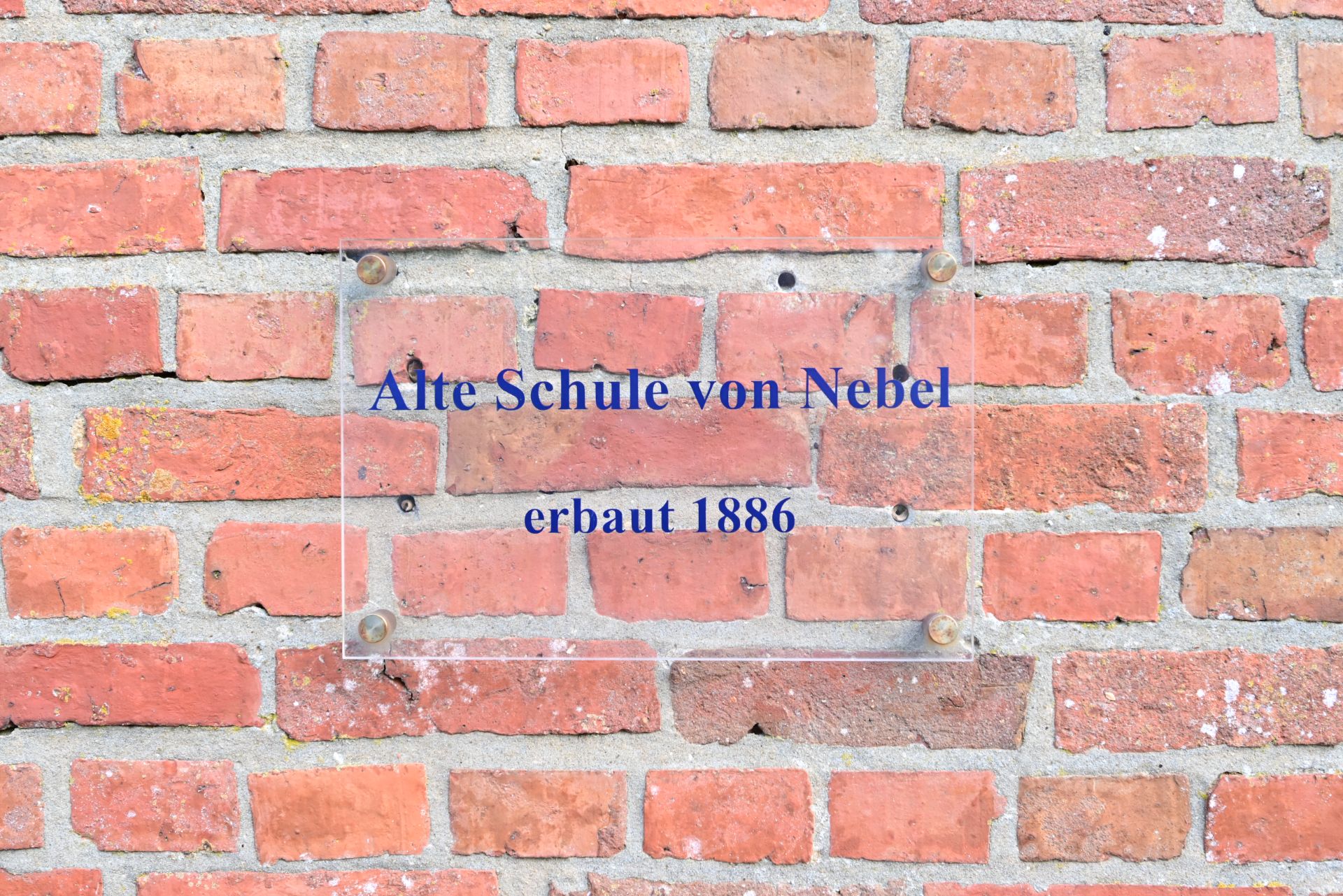Klinkerwand mit einem Schild, auf dem 'Alte Schule von Nebel, erbaut 1886' steht.