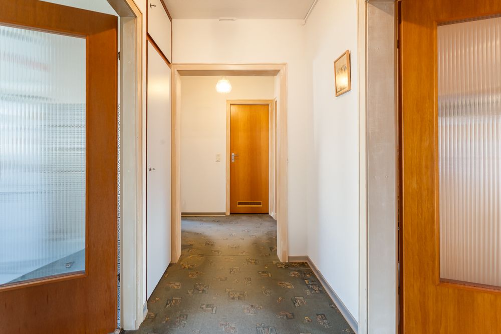 Heller Flur mit Teppichboden, Holztüren und Wandschrank in einer Wohnung.