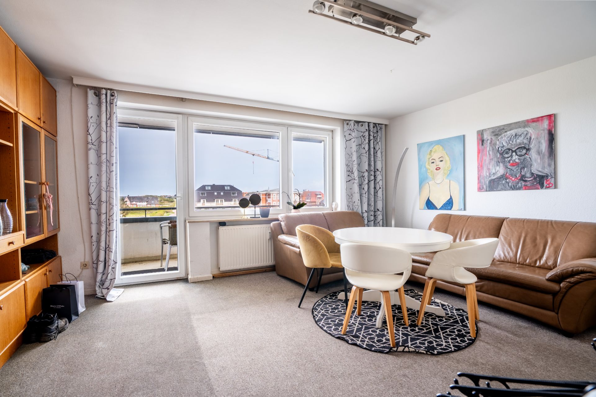 Helles Wohnzimmer mit braunem Sofa, rundem Tisch, Stühlen und Balkonzugang.