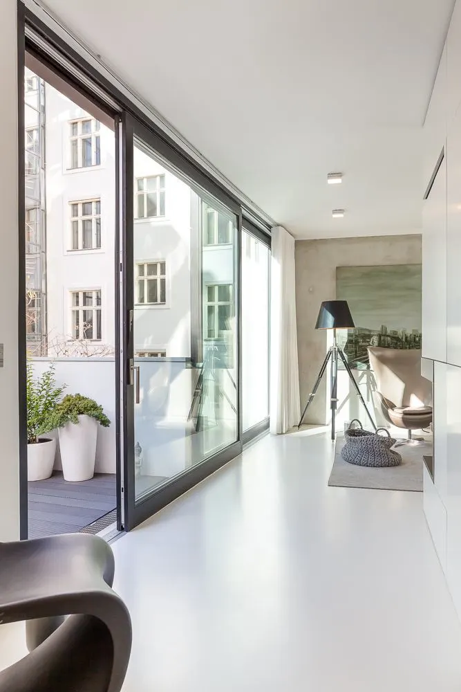 Helles Wohnzimmer mit großen Glas-Schiebetüren zu einem Balkon mit Pflanzen in weißen Töpfen.
