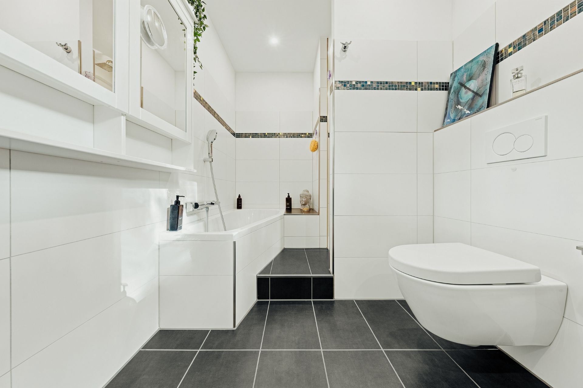 Modernes Badezimmer mit Badewanne, Hängetoilette und weißen Fliesen, schwarze Bodenfliesen.