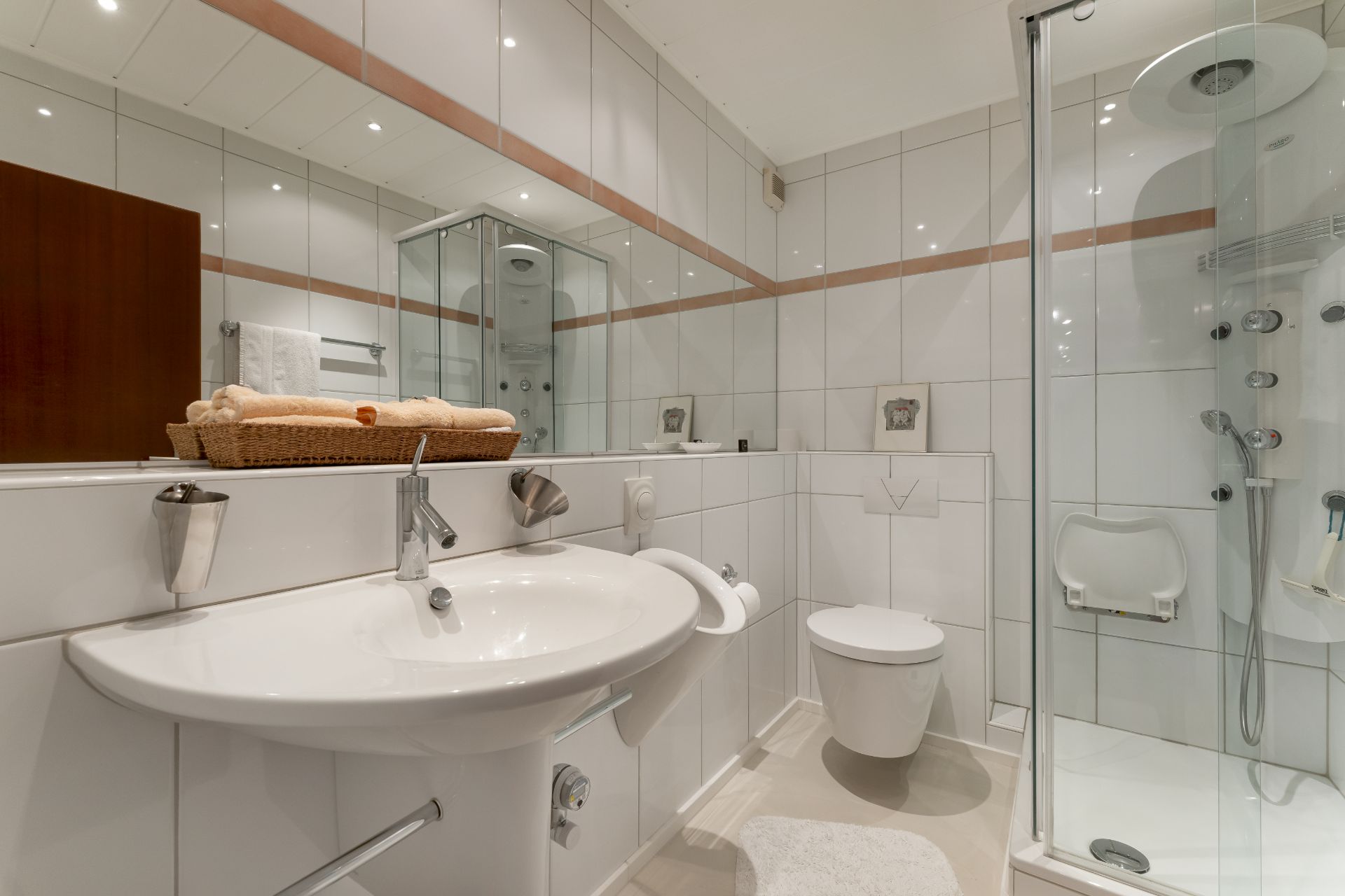 Modernes Badezimmer mit Waschbecken, Spiegel, Dusche und WC, weiße Fliesen an Wand und Boden.