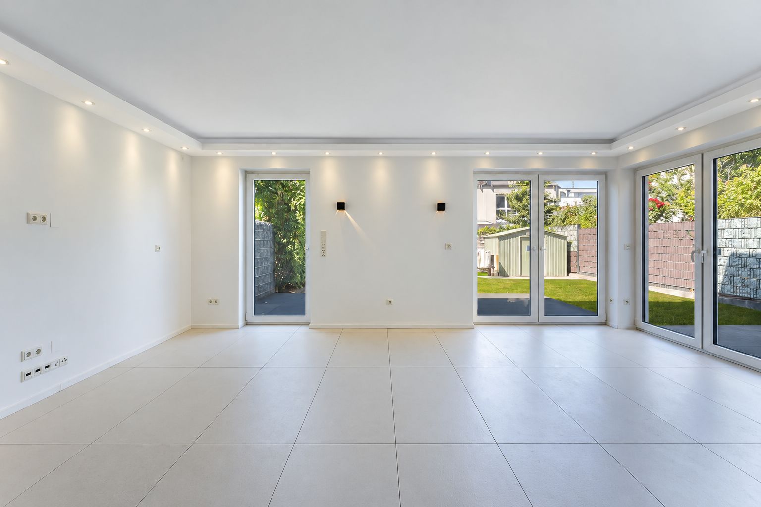 Helles, leeres Wohnzimmer mit großen Fenstern und Blick in den Garten.