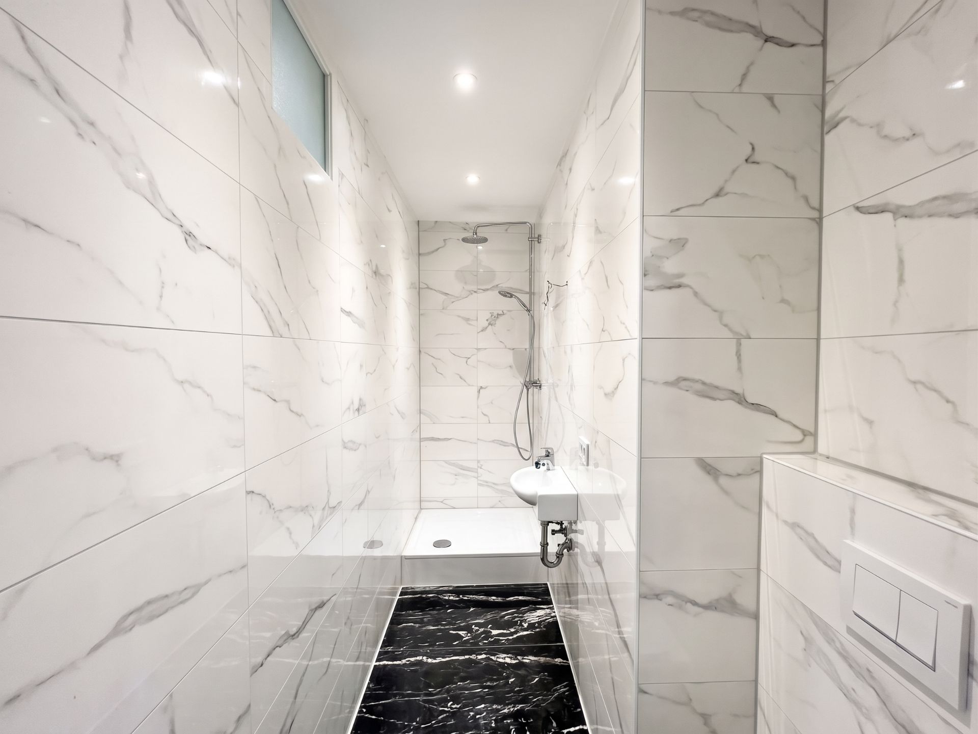 Modernes Bad mit Marmorfliesen, begehbarer Dusche und kleinem Waschbecken.