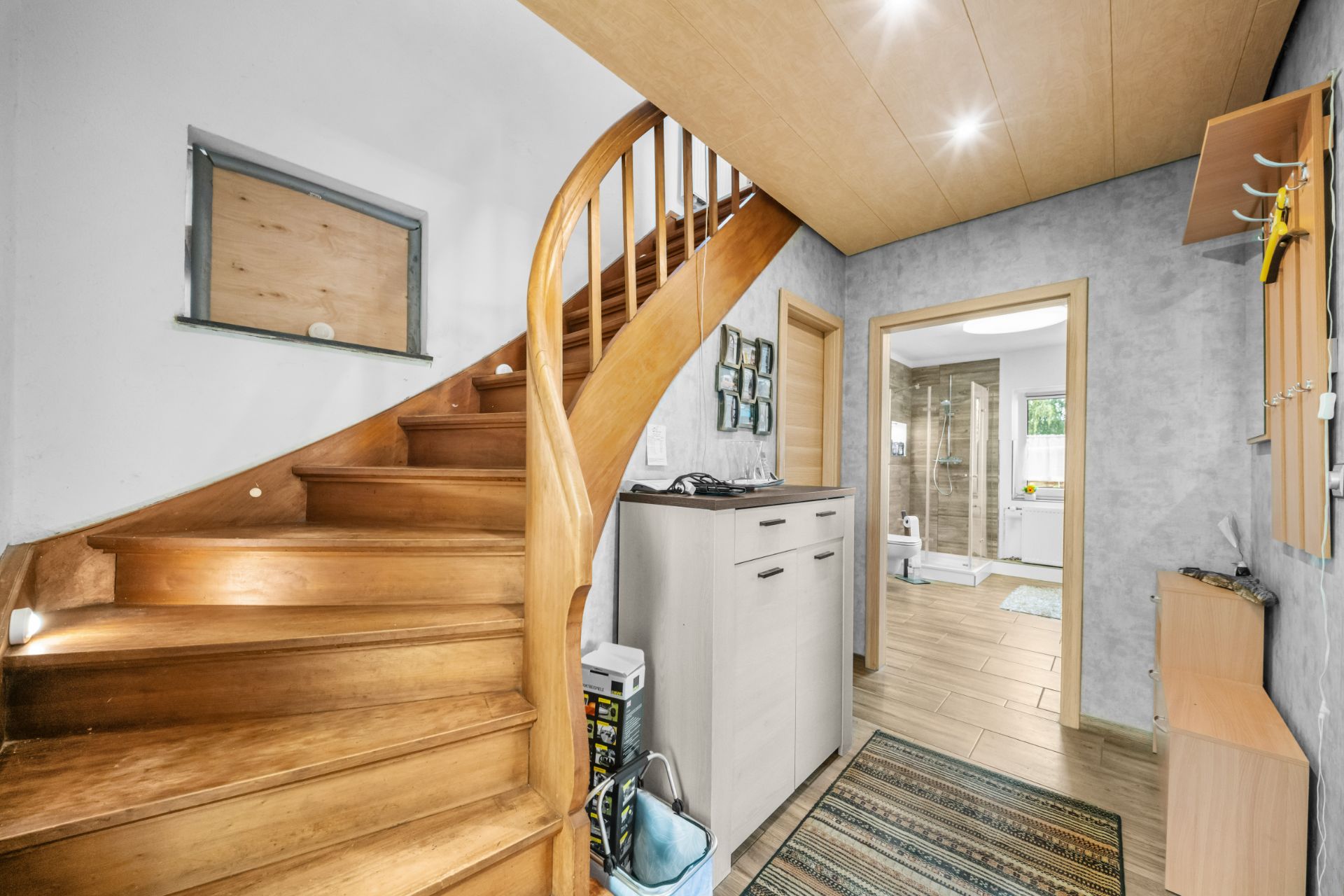 Flur mit Holztreppe, Kommode, Garderobe und Blick ins Badezimmer.