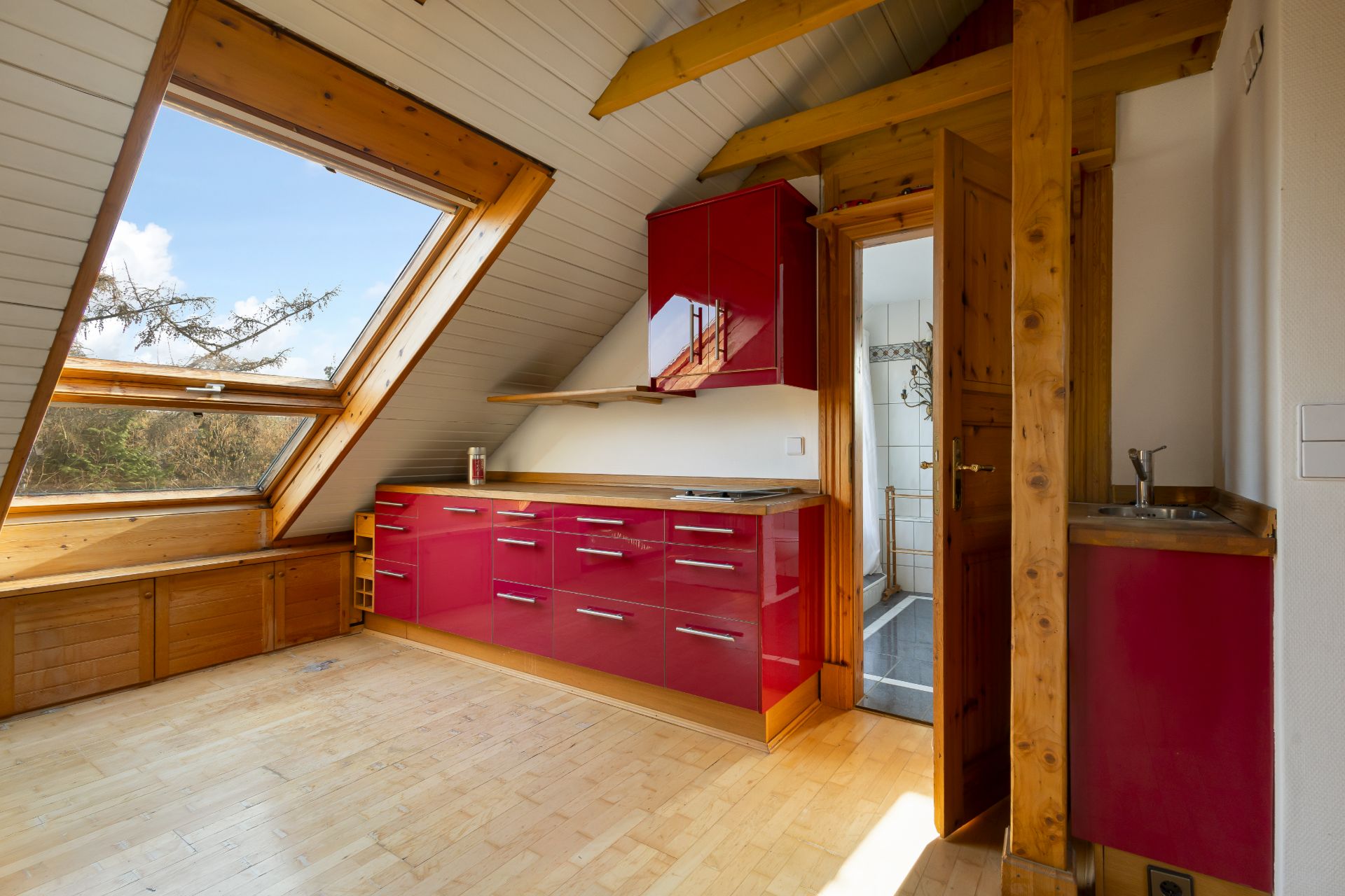 Helle Dachgeschossküche mit roten Schränken, großem Fenster und Holzbalken.
