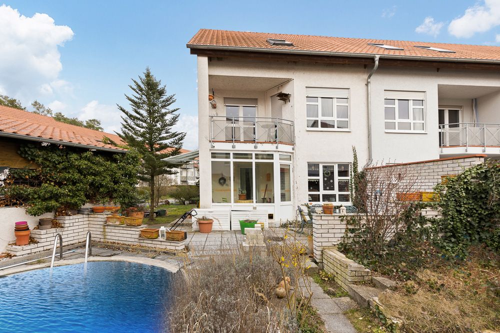 Zweistöckiges Wohnhaus mit Balkon, Terrasse, Pool und Garten mit Blumentöpfen.