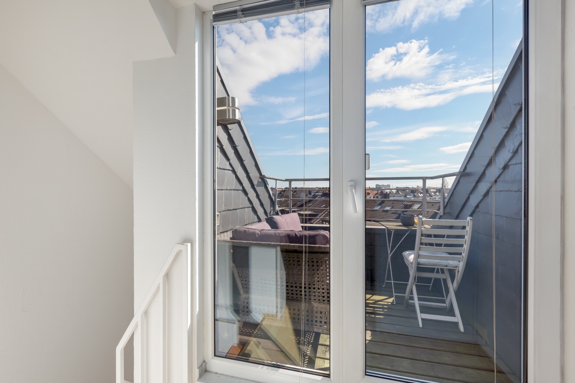 Blick durch Glastür auf einen kleinen Balkon mit Stühlen und Tisch.