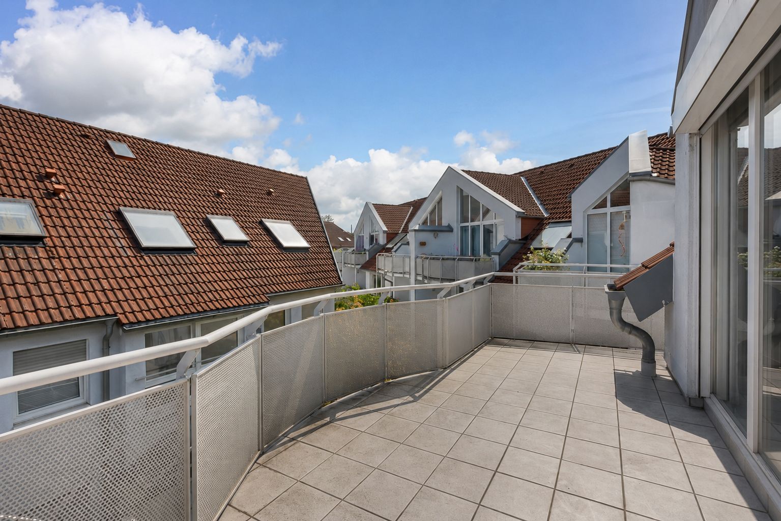 Großer Balkon mit Fliesenboden, Blick auf Nachbarhäuser mit roten Dächern und Dachfenstern.