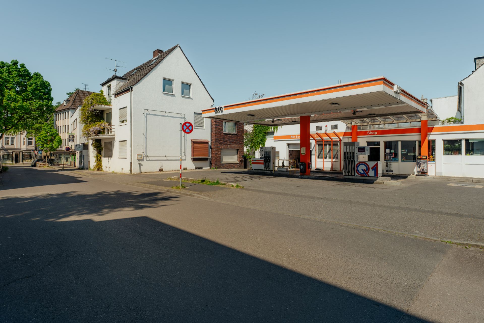 Wohnhäuser neben einer Tankstelle an einer Straßenecke bei klarem Himmel.