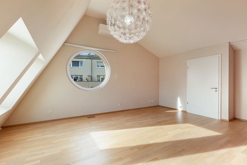 Helles Zimmer mit rundem Fenster, Holzboden und moderner Hängelampe.