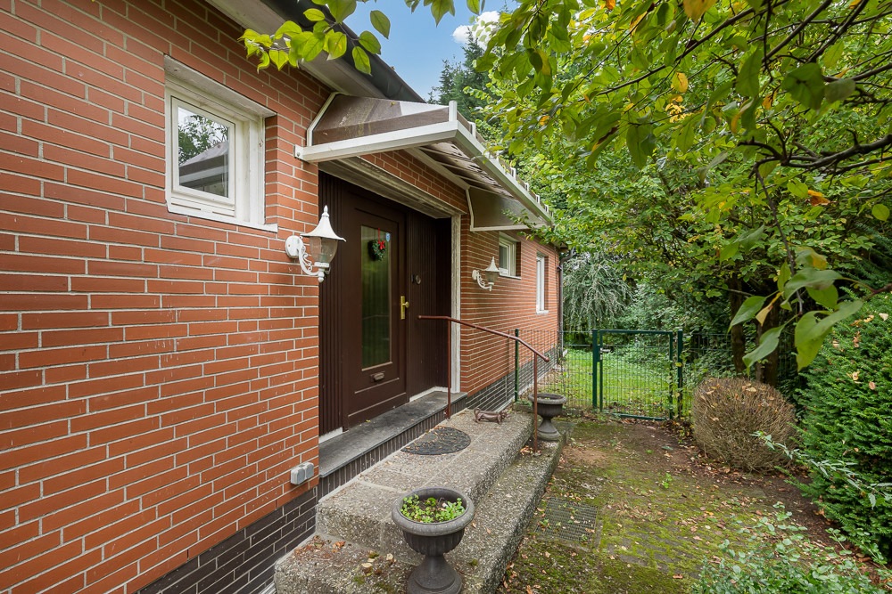 Eingang eines Backsteinhauses mit brauner Tür, zwei Lampen und Garten rundherum.