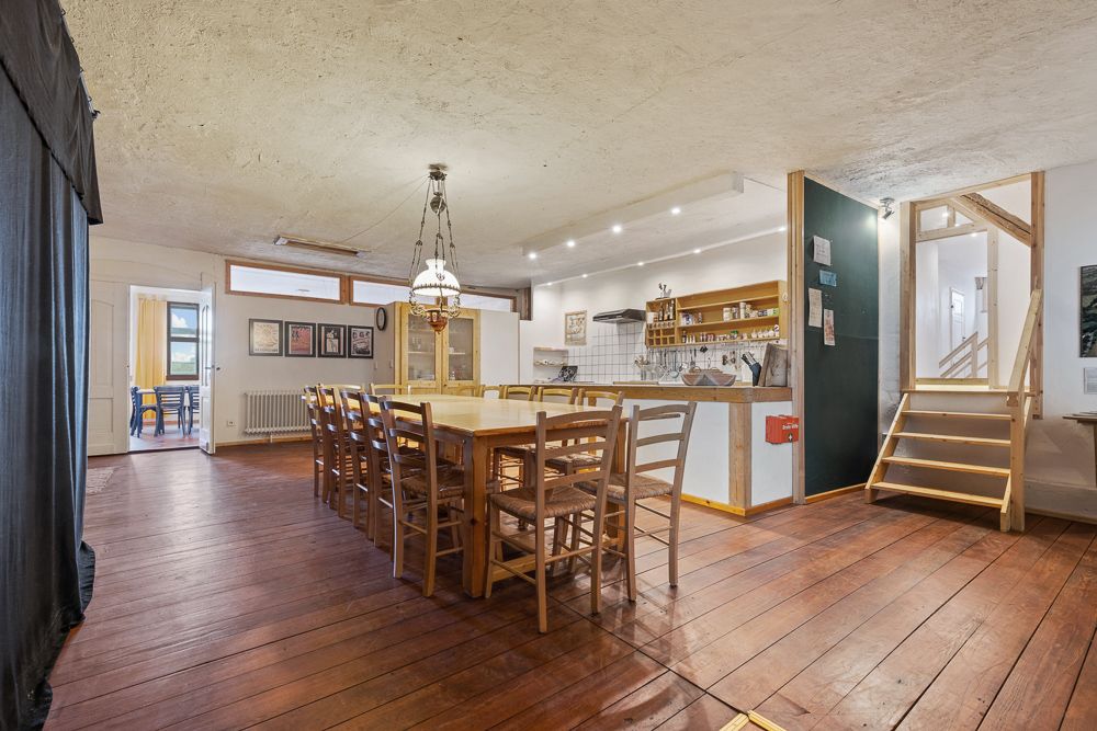 Großer Essbereich mit langem Holztisch, Stühlen und offener Küche auf Holzfußboden.