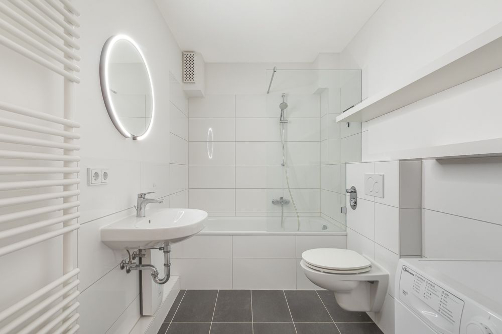 Modernes Badezimmer mit Badewanne, beleuchtetem Spiegel, Waschbecken und Wand-WC.