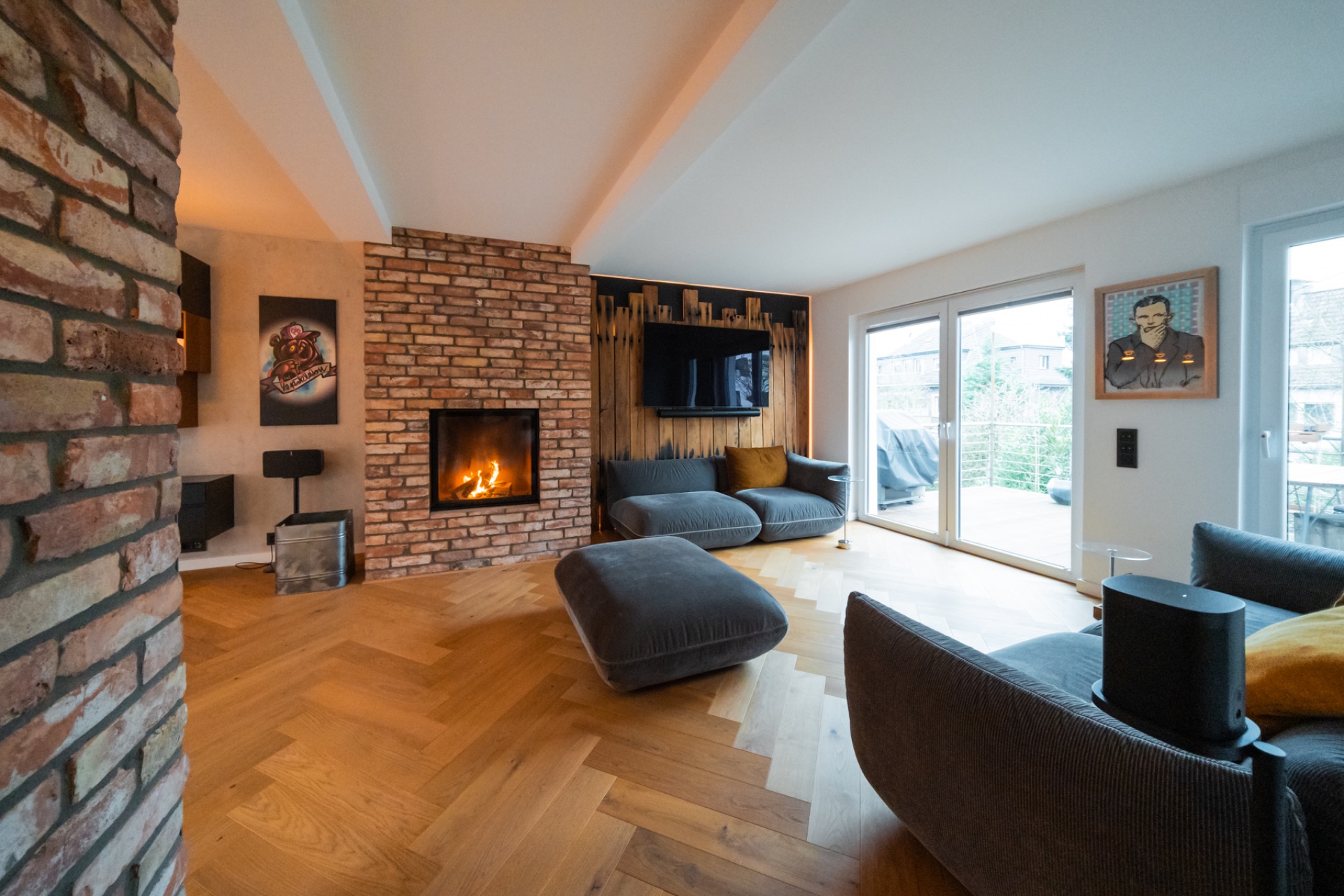 Modernes Wohnzimmer mit Kamin, grauen Sofas, Holzboden und Zugang zur Terrasse.