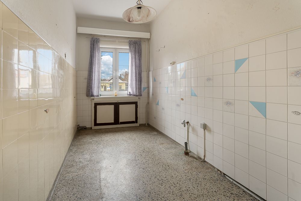 Leerer, schmaler Raum mit gefliestem Wänden, Fenster am Ende und sichtbaren Wasseranschlüssen.