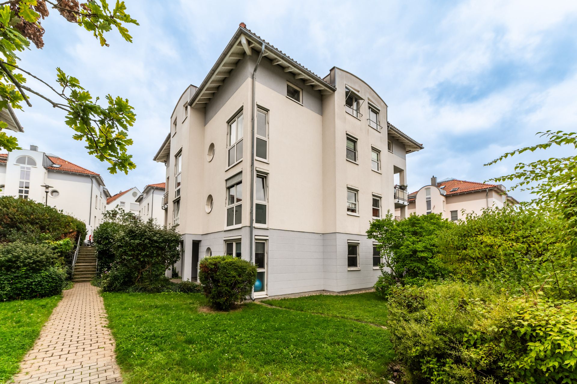 Mehrstöckiges Wohnhaus mit hellen Fassaden und gepflegtem Garten im Vordergrund.