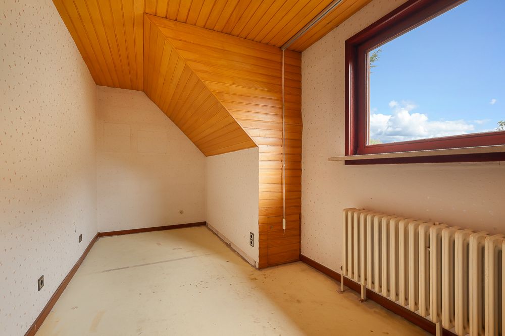 Kleines leeres Zimmer mit Dachschräge, Holzdecke, Fenster und Heizkörper.