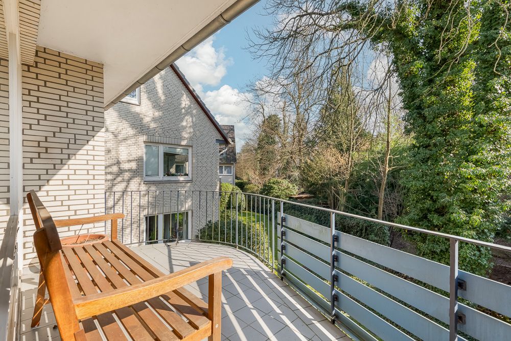 Balkon mit Holzbank, Blick auf Garten und Nachbarhaus mit Klinkerfassade.