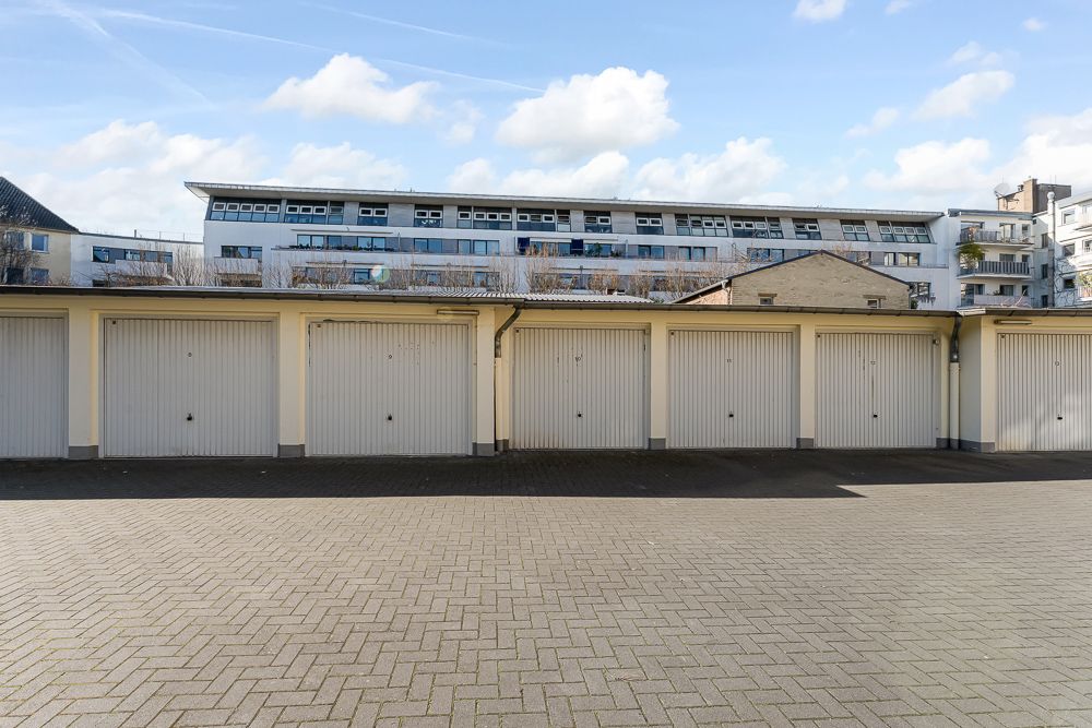 Reihe geschlossener Garagentore vor einem Mehrfamilienhaus bei Tageslicht.