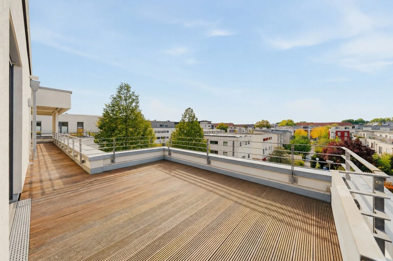 Große Dachterrasse mit Holzbelag und Blick auf Bäume und Wohngebäude.