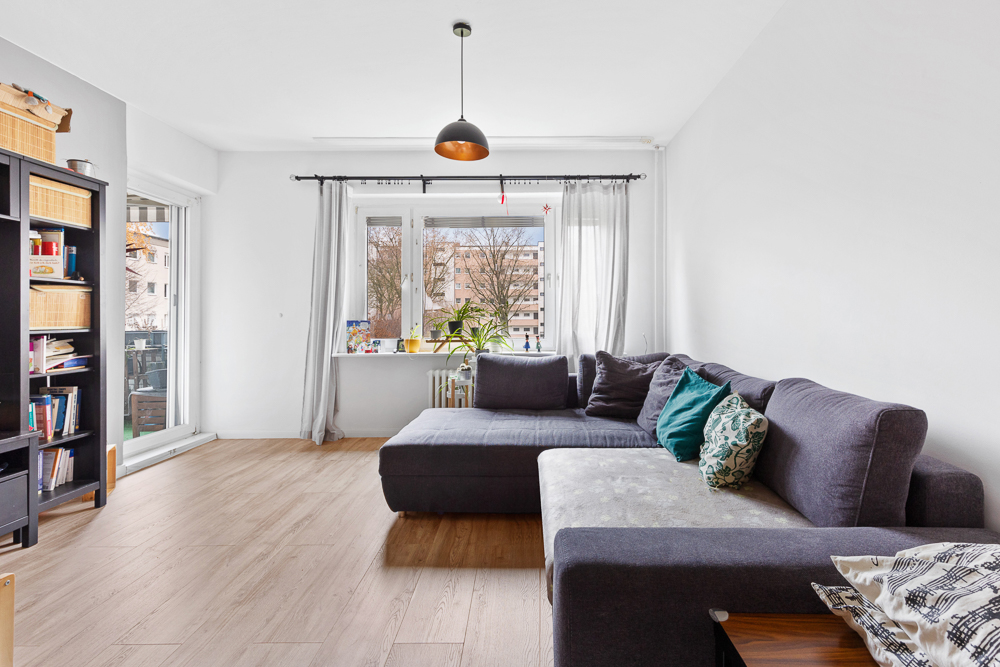Helles Wohnzimmer mit großer grauer Eckcouch, Bücherregal und Fenster mit Blick nach draußen.