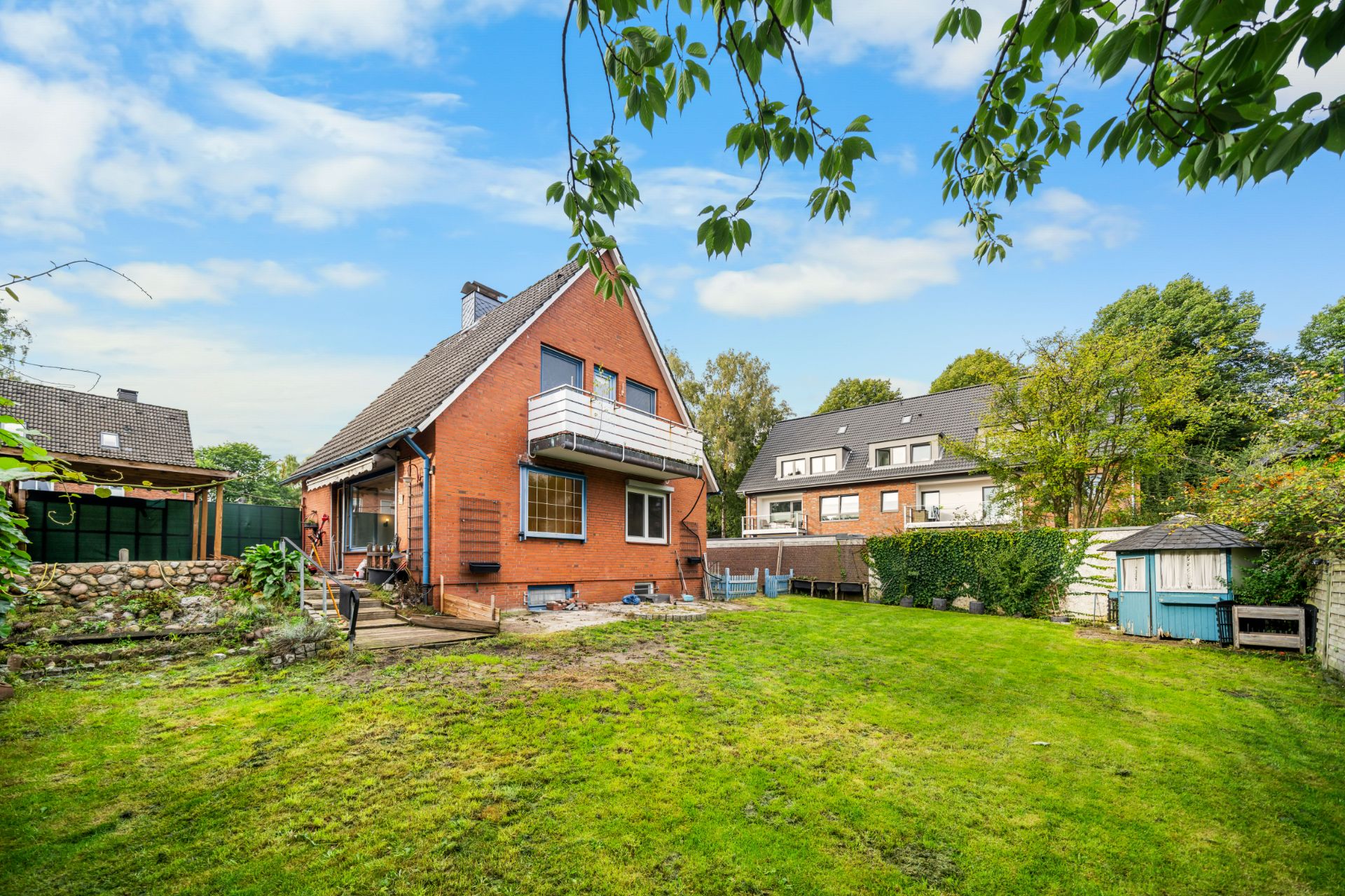 Ein rotes Einfamilienhaus mit Balkon steht in einem großen grünen Garten.