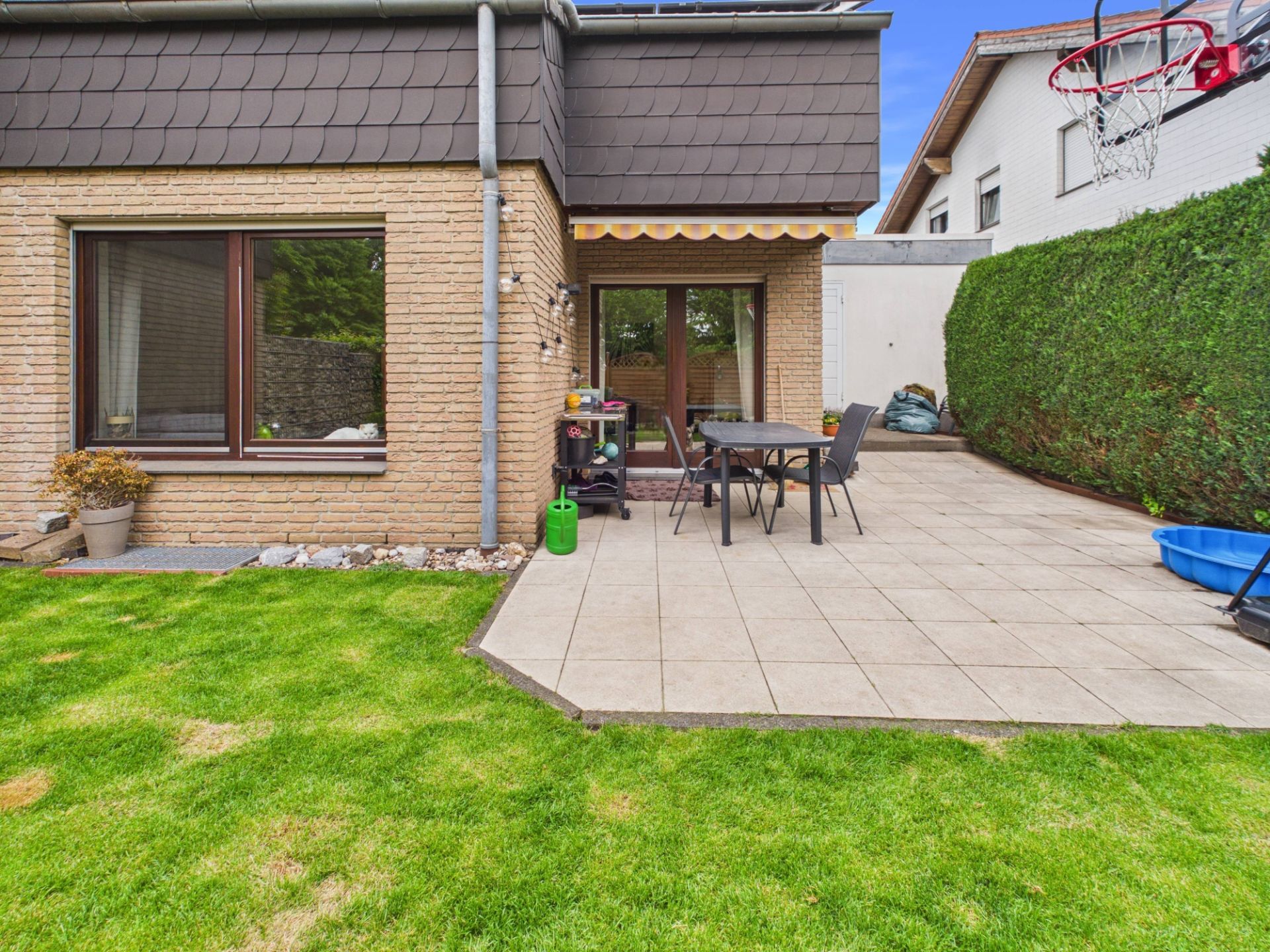 Gepflegter Garten mit Terrasse, Tisch und Stühlen an einem Wohnhaus.