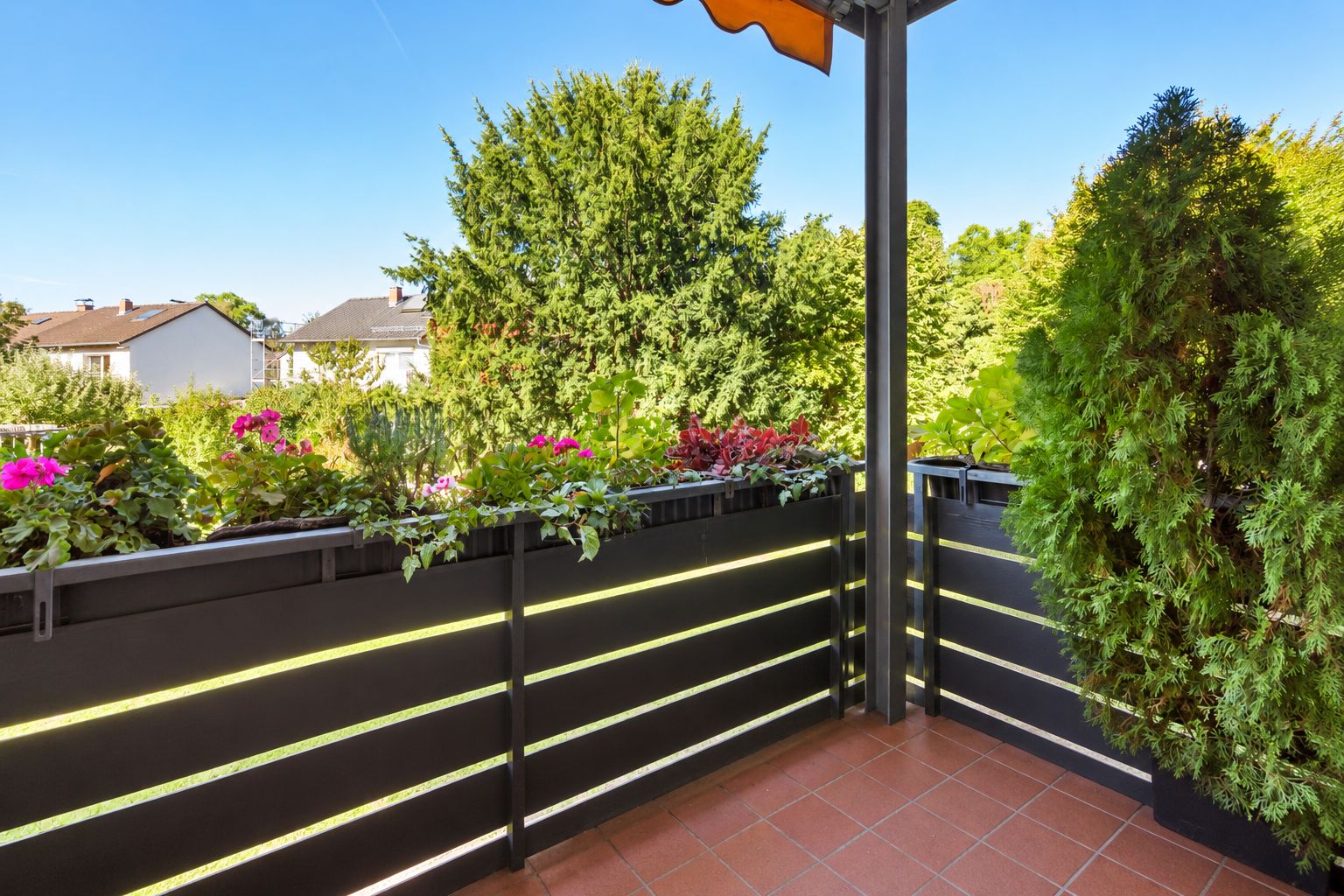 Balkon mit schwarzen Geländern, Blumentöpfen und Blick auf grüne Bäume.