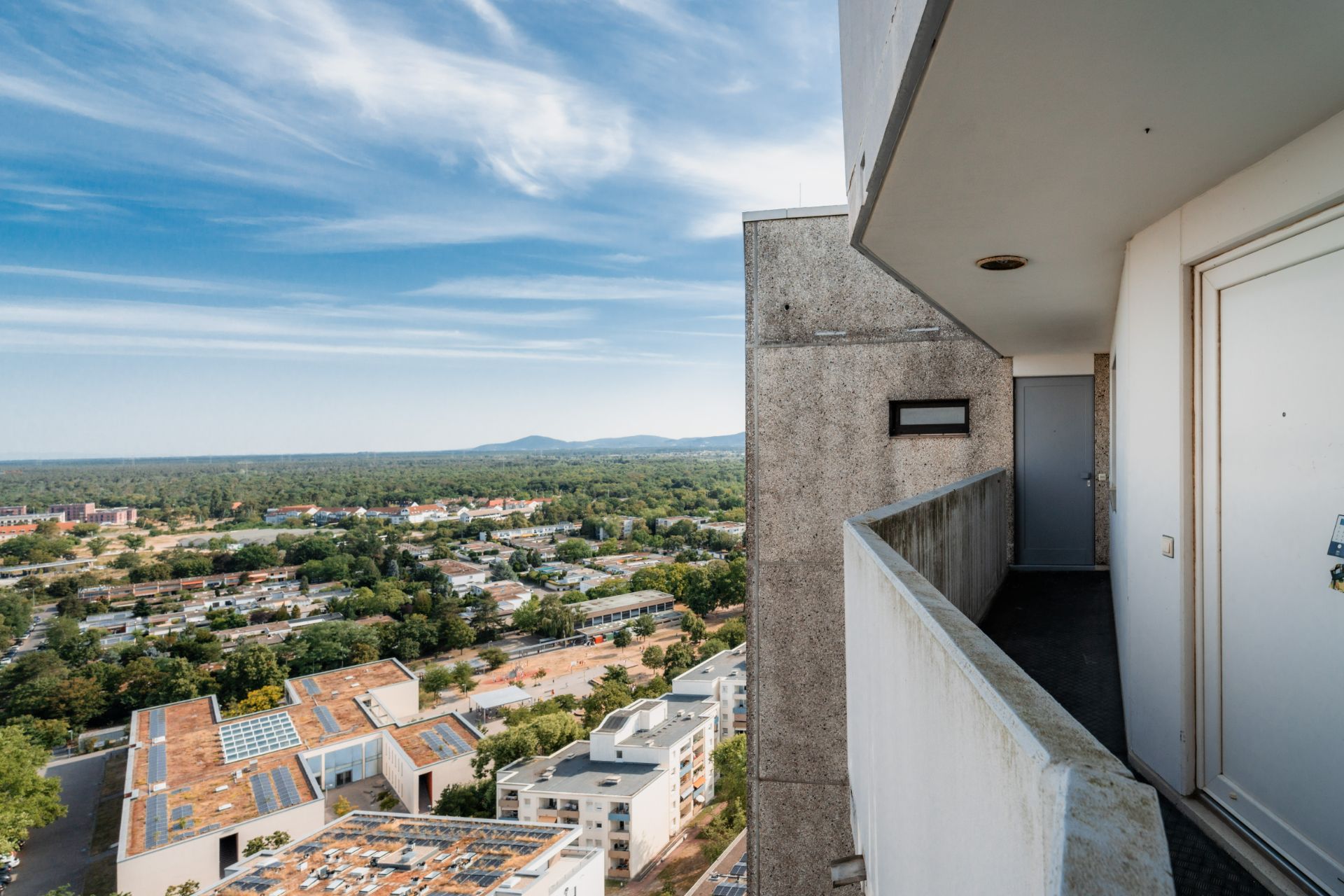 Blick von einem Wohnhausbalkon auf eine Stadt mit Bäumen und Häusern im Hintergrund.
