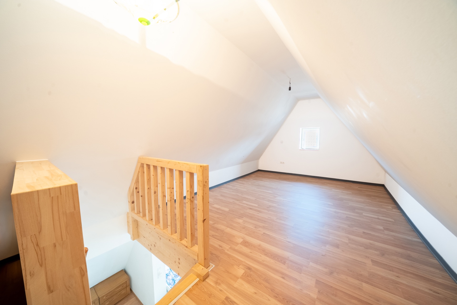 Heller Dachbodenraum mit Holztreppe und Fenster, leer und mit Holzfußboden.