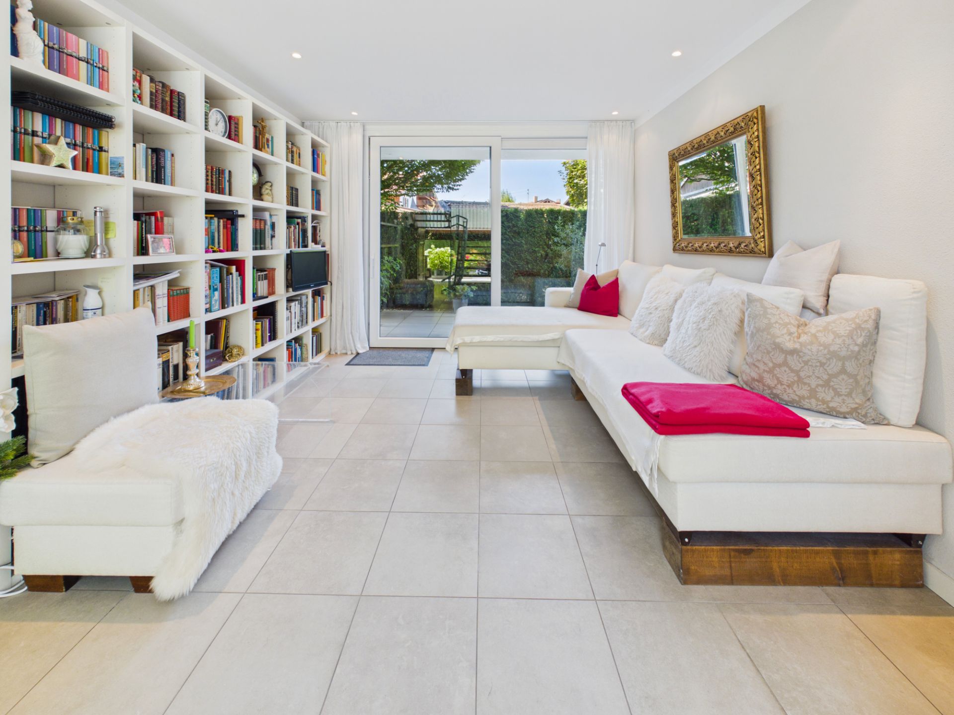 Helles Wohnzimmer mit weißer Eckcouch, Bücherregal und Glastür zum Garten.
