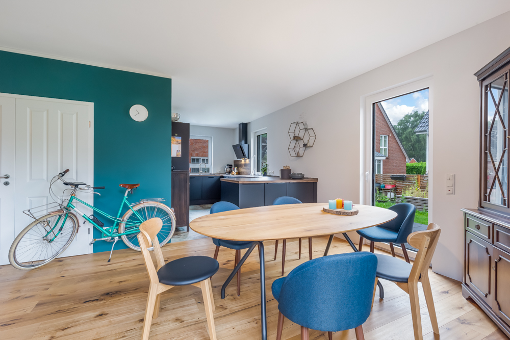 Heller Essbereich mit Holztisch, bunten Stühlen, Fahrrad an wand, Zugang zur Terrasse und moderner Küche.