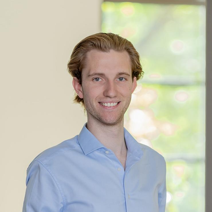 Eine Person in einem hellblauen Hemd steht vor einem Fenster mit unscharfem Hintergrund.