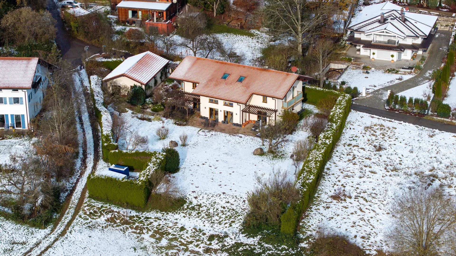 Luftaufnahme eines Hauses mit rotem Dach und Garten, umgeben von leicht verschneitem Grundstück.