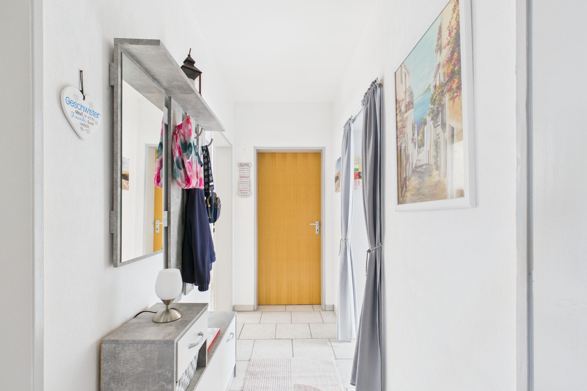 Heller Flur mit Garderobe, Spiegel, Wandbild und gelber Tür am Ende.